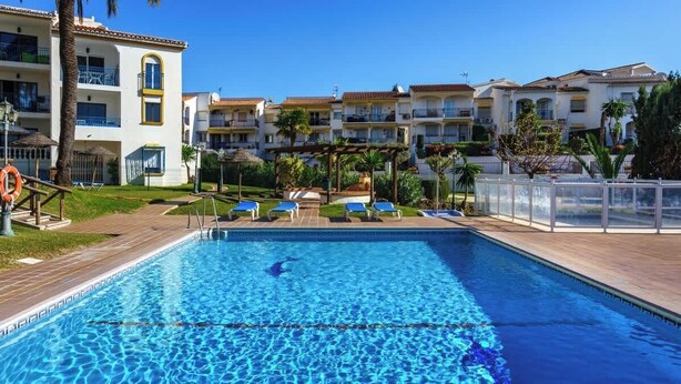 A swimming pool with lounge chairs and a lifebuoy, surrounded by apartment buildings with balconies and a clear sky. - Miraflores with pool by Costarentals - Ref 146 (Las Lagunas de Mijas)