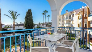 A balcony with a white table set for two, overlooking a residential area with palm trees and a clear blue sky. - Miraflores with pool by Costarentals - Ref 146 (Las Lagunas de Mijas)