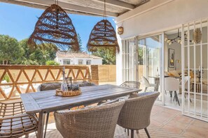 An outdoor patio with a wooden table and wicker chairs, a decorative hanging light, and a view of a white building in the background. - Townhouse with Pool by Costarentals- Ref 199 (Las Lagunas de Mijas)