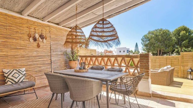Eine Terrasse im Freien mit einem Holztisch, Korbstühlen und einer gepolsterten Sitzecke.