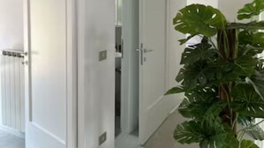 A hallway with white walls and doors, leading to a room with a potted plant. - TERRACE VIEW FLORENCE ATTIC (Firenze)
