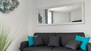 A modern living room with a dark grey sofa, teal cushions, a large mirror, and a decorative wall piece. - TERRACE VIEW FLORENCE ATTIC (Firenze)
