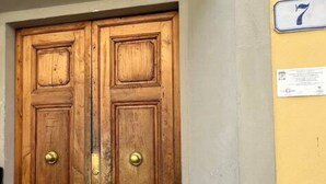 A wooden double door with brass handles, a yellow wall with a number '7' sign, and a small notice board. - TERRACE VIEW FLORENCE ATTIC (Firenze)