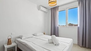 Ein Schlafzimmer mit einem Bett, einem Nachttisch, einer Korblampe und einem Fenster mit Vorhängen.