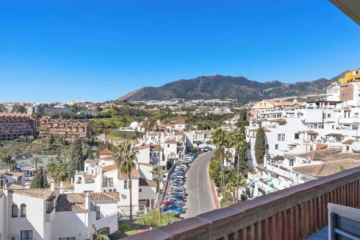 Un pueblo costero con edificios blancos, una carretera curva y una montaña al fondo.