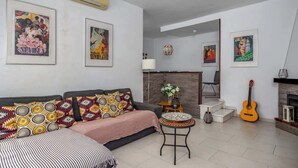 Ein Wohnzimmer mit einer Couch, einem kleinen Tisch und einer Gitarre. An den Wänden befinden sich Bilder in Rahmen und ein Kamin.