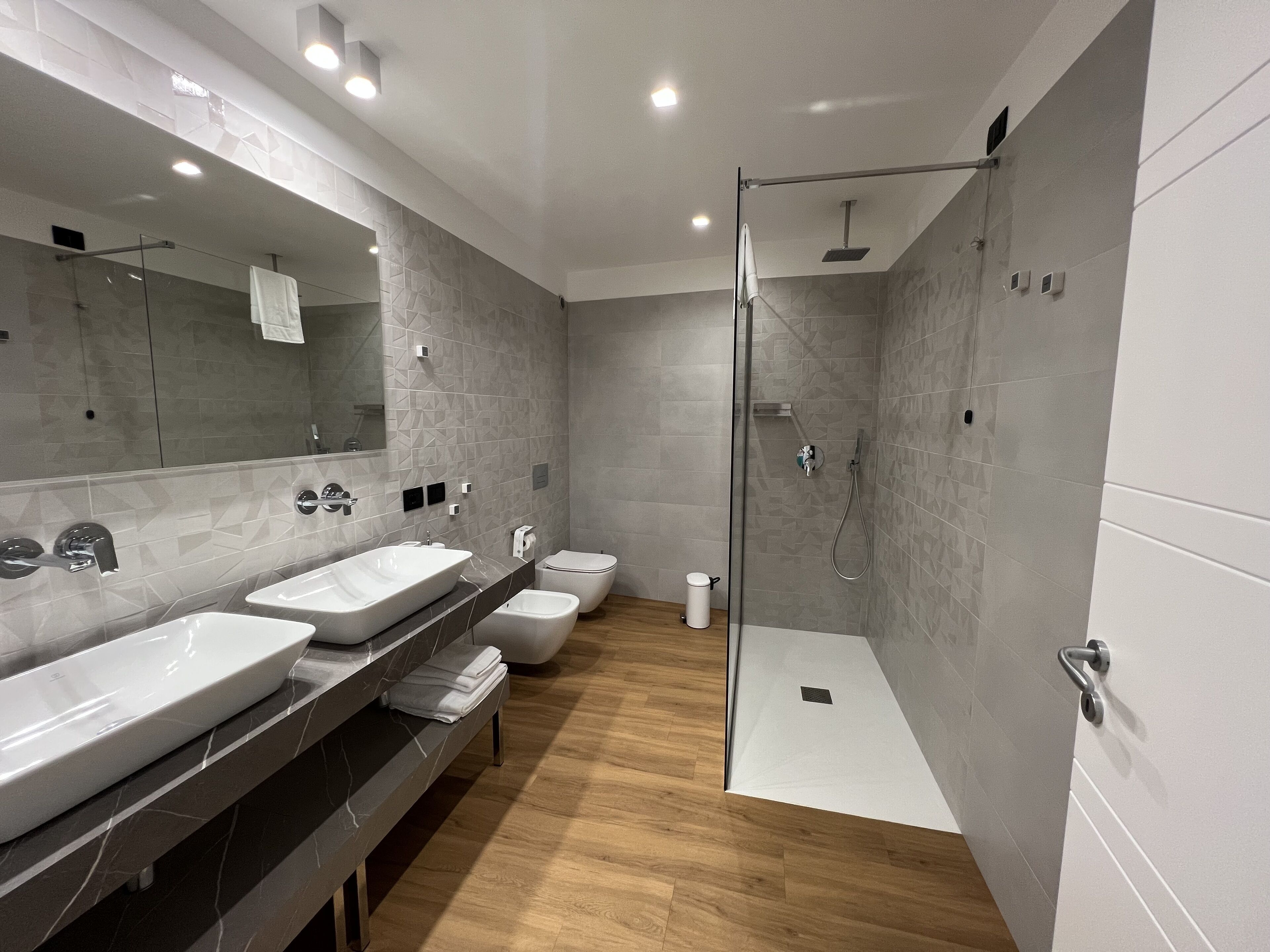 Une salle de bain moderne avec deux lavabos, des toilettes et une douche séparée par une paroi en verre.