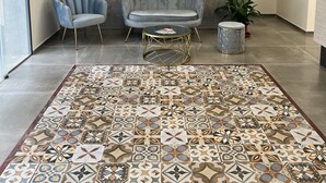 Un salon moderne avec un tapis à motifs, deux fauteuils, une table basse ronde et un grand tableau abstrait accroché au mur.
