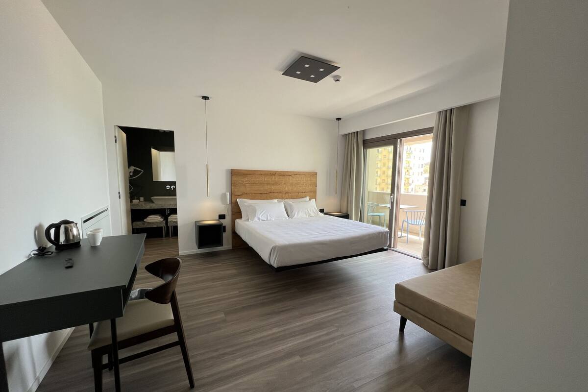 Una habitación de hotel moderna con cama, escritorio, silla, una mesita pequeña y un balcón con vistas.