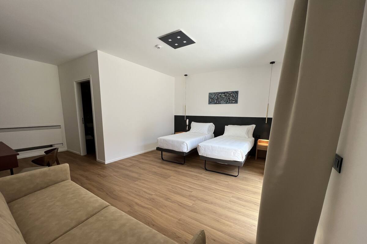 Una habitación de hotel moderna con dos camas individuales, piso de madera, un escritorio pequeño y una silla.