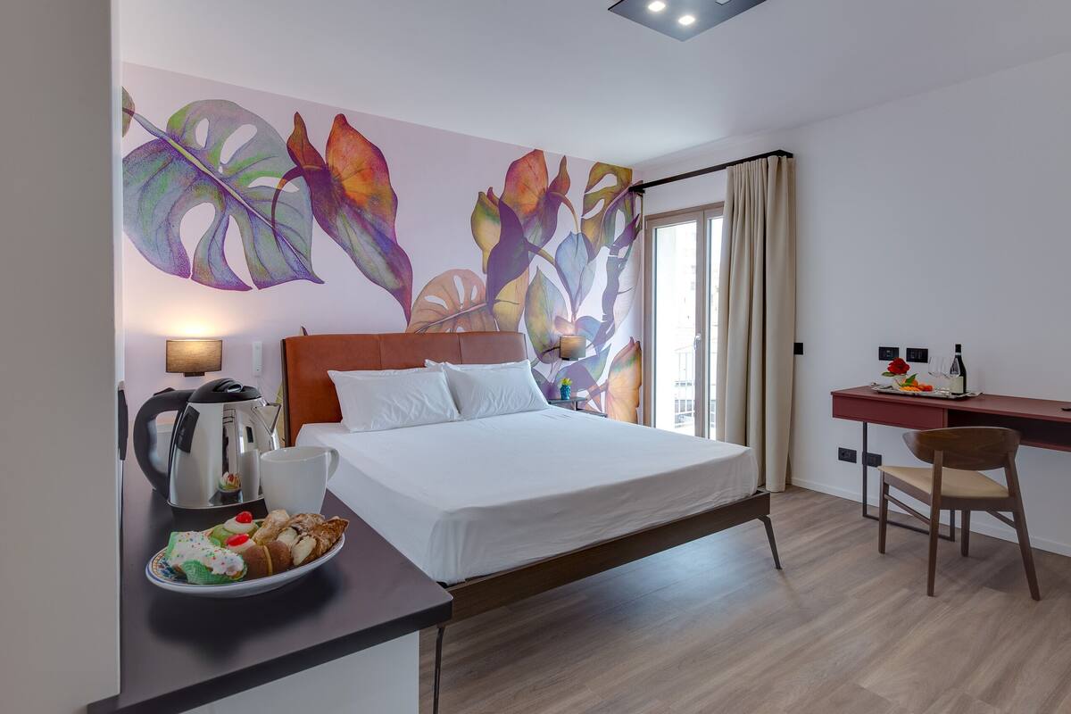 Una habitación de hotel moderna con una cama, un escritorio y un ventanal grande.