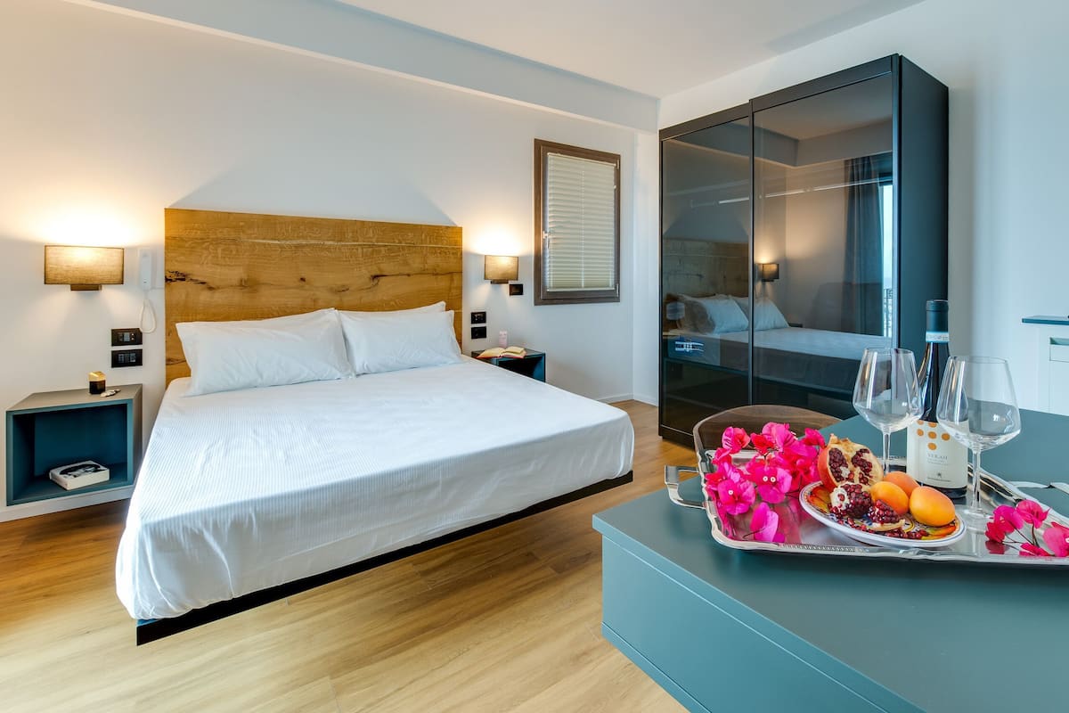 Habitación de hotel moderna con cama de cabecera de madera, mesitas de noche con lámparas, un espejo grande y una bandeja con comida y bebidas.