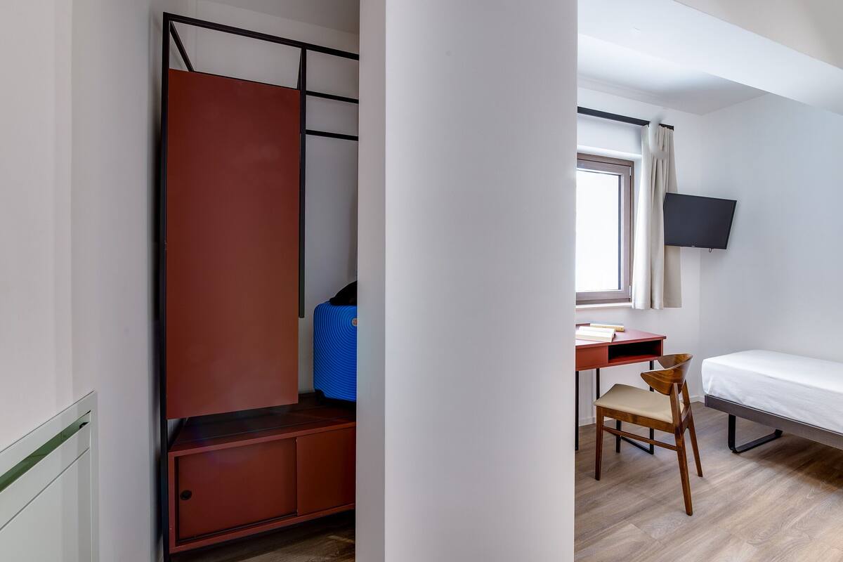 Una habitación pequeña con cama, escritorio, silla, televisor y armario.