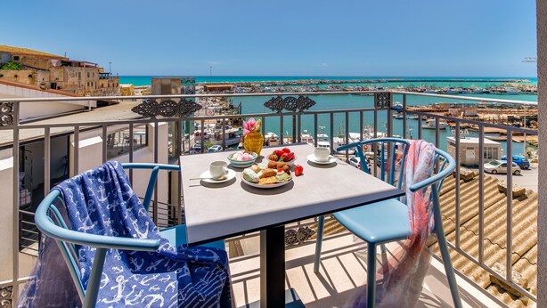 Un balcon avec une table préparée pour le petit-déjeuner, d’où l’on peut admirer une ville côtière et la mer.