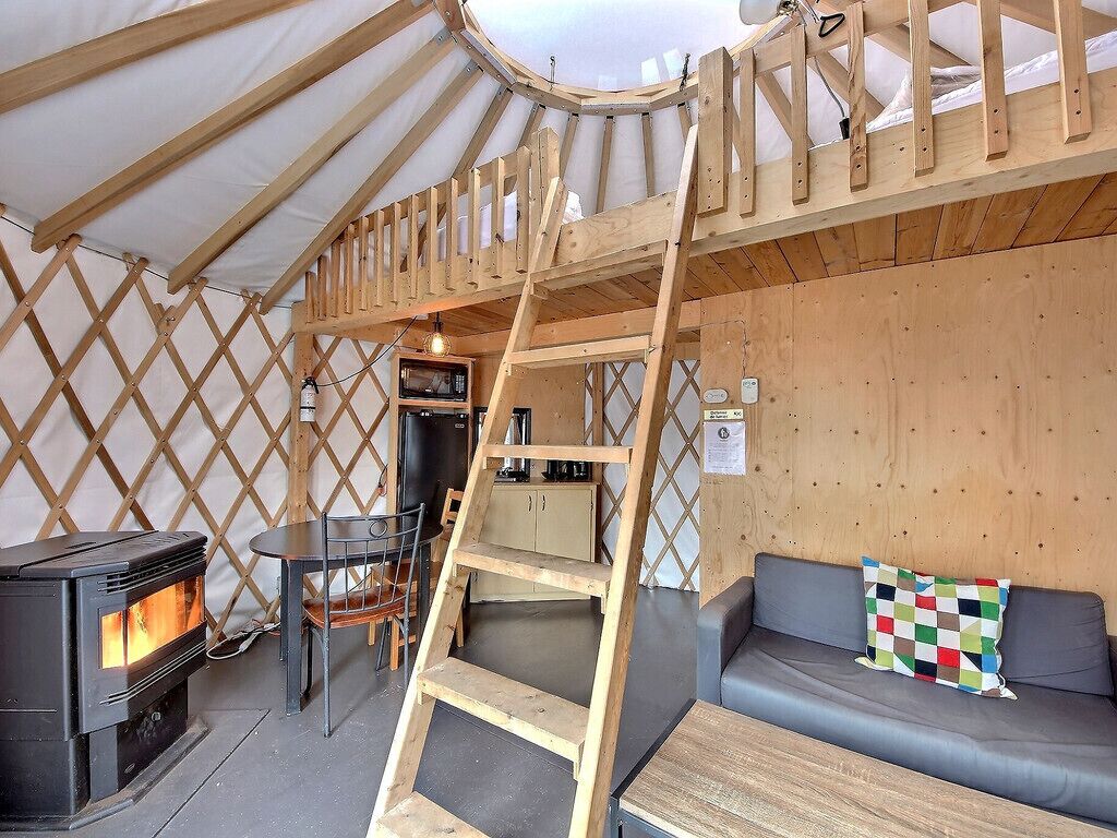 Un interior acogedor con una escalera de madera, un sofá, una mesa, una estufa y una pequeña cocina.