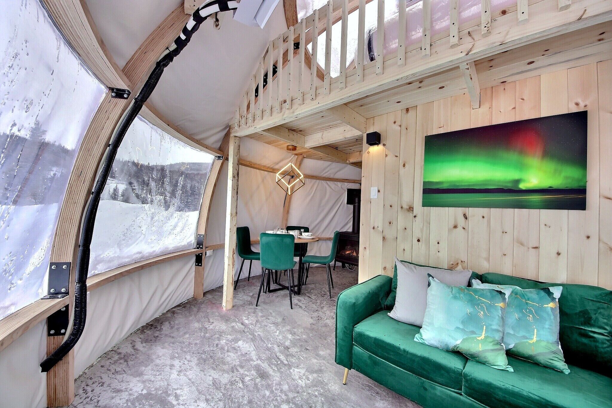 A cozy interior with a green sofa, a dining table with chairs, and a painting of the Northern Lights.