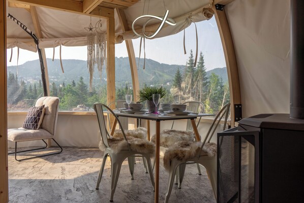 A cozy dining area with a table set for two, chairs, a television, and a scenic mountain view. - Imago Village (Saint-David-de-Falardeau)