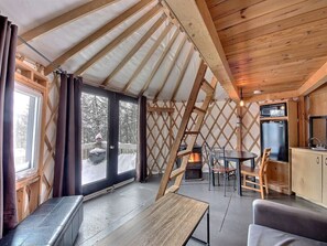 A yurt interior with a wooden ceiling, a fireplace, a dining area, and a kitchen. - Imago Village (Saint-David-de-Falardeau)