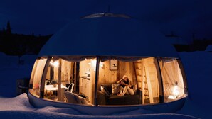 Igloo cubierto de nieve con un interior cálido, paredes de madera y un juego de mesa y sillas.
