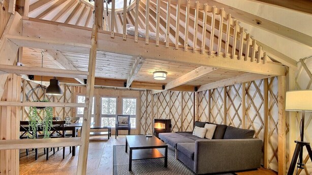 Un interior acogedor de cabaña con una escalera de madera, un sofá, una mesa de comedor y una chimenea.