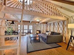 Un interior acogedor de cabaña con una escalera de madera, un sofá, una mesa de comedor y una chimenea.