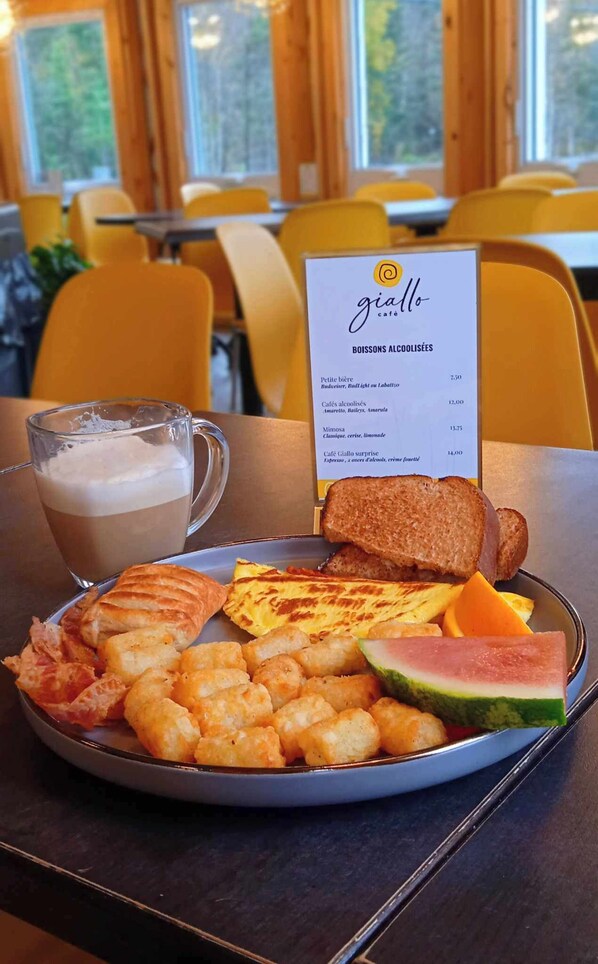 Un plato de desayuno con tostadas, camarones, nuggets de papa y una porción de sandía, acompañado de una taza de café.