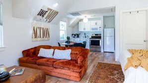 Ein modernes Wohnzimmer mit einem roten Samtsofa, einem Holztisch und einer Küche im Hintergrund.