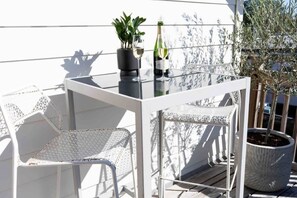 A balcony with a glass table, two potted plants, a bottle of wine, and white outdoor furniture. - mid-century 70s retro studio, walk to restaurants (Houston)