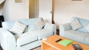 Un salon avec deux canapés bleu clair, une table basse en bois, une télécommande et un livre vert.
