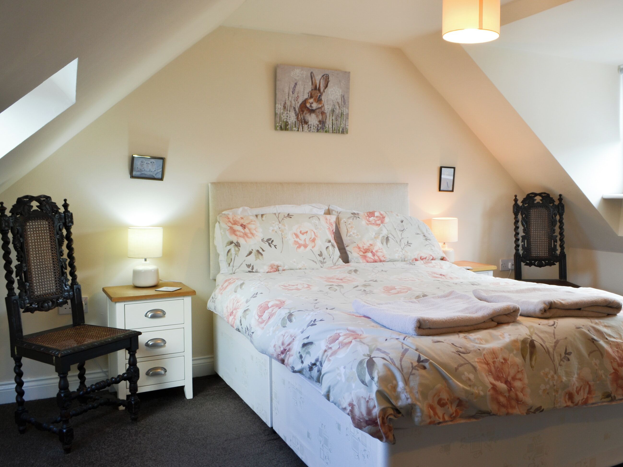 Una camera da letto con un letto, due comodini, una sedia e un quadro appeso al muro.