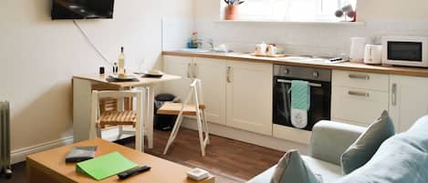 A modern kitchen with a dining area, a TV mounted on the wall, and a window with a view.