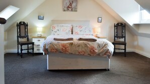 Une chambre à coucher comprenant un lit, deux tables de chevet, deux chaises, un luminaire au plafond et un tableau mural.