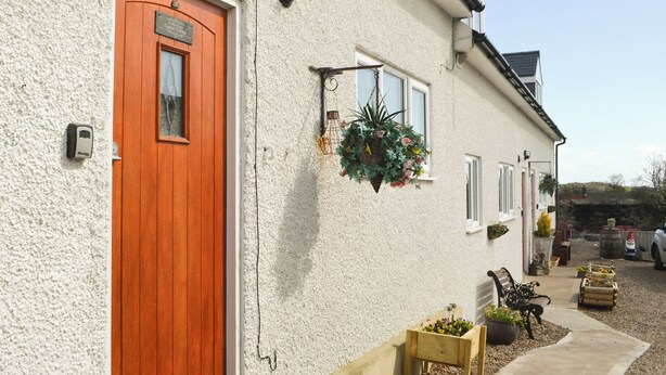 Un bâtiment avec une porte en bois, une jardinière suspendue et un banc à l’extérieur.