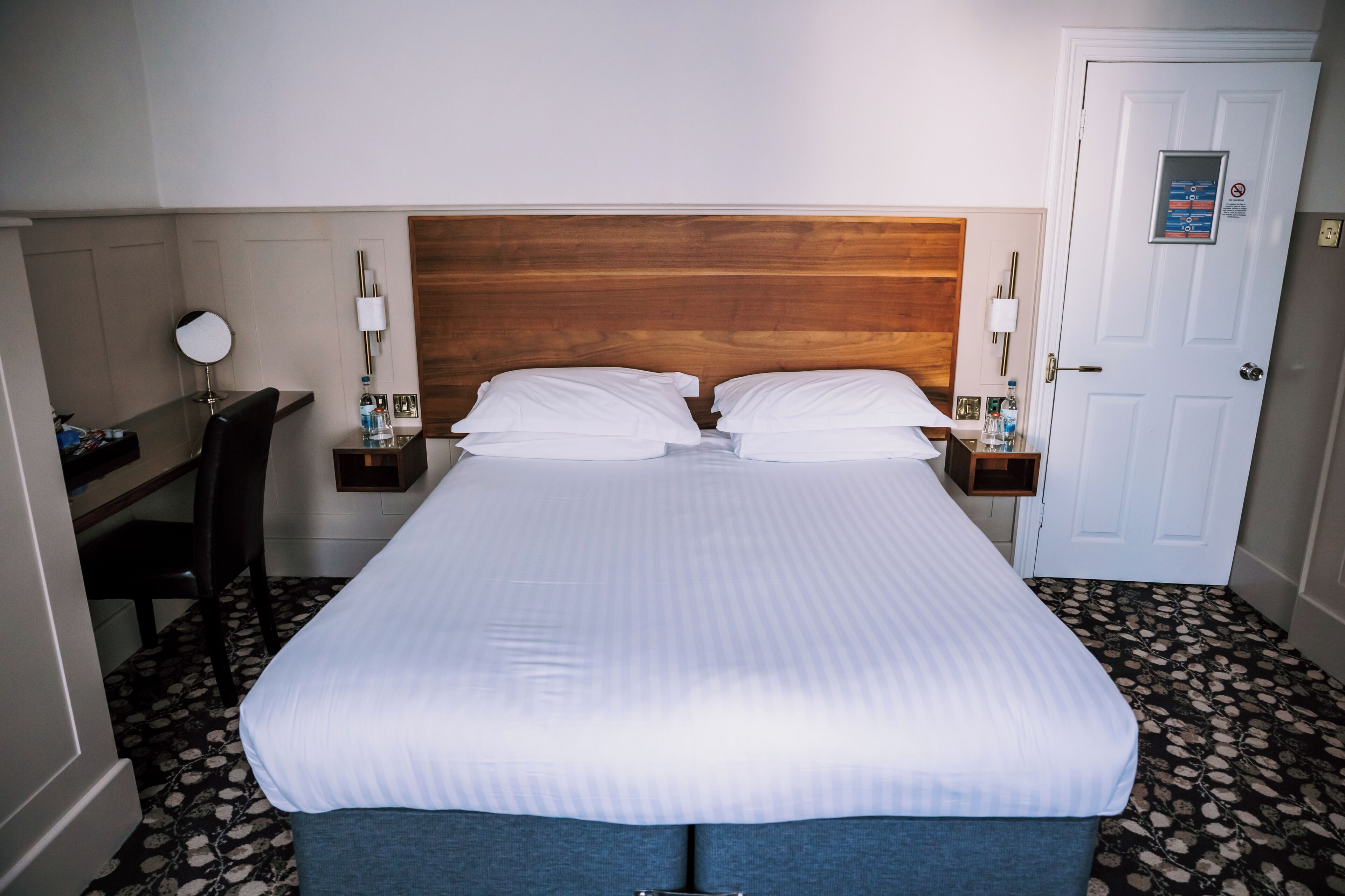 Una habitación de hotel con cama, mesitas de noche, escritorio, silla y puerta.