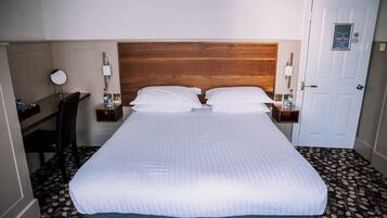 Una habitación de hotel con cama, mesitas de noche, escritorio, silla y puerta.