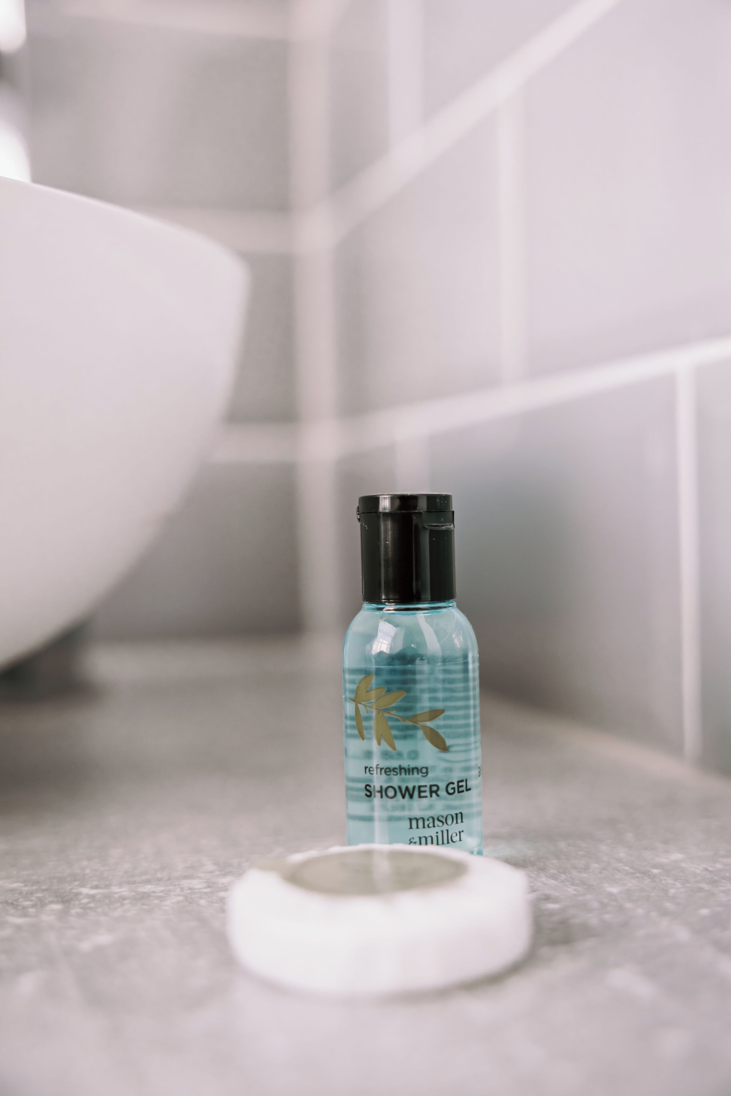 Une salle de bain avec un flacon de gel douche posé sur le sol.