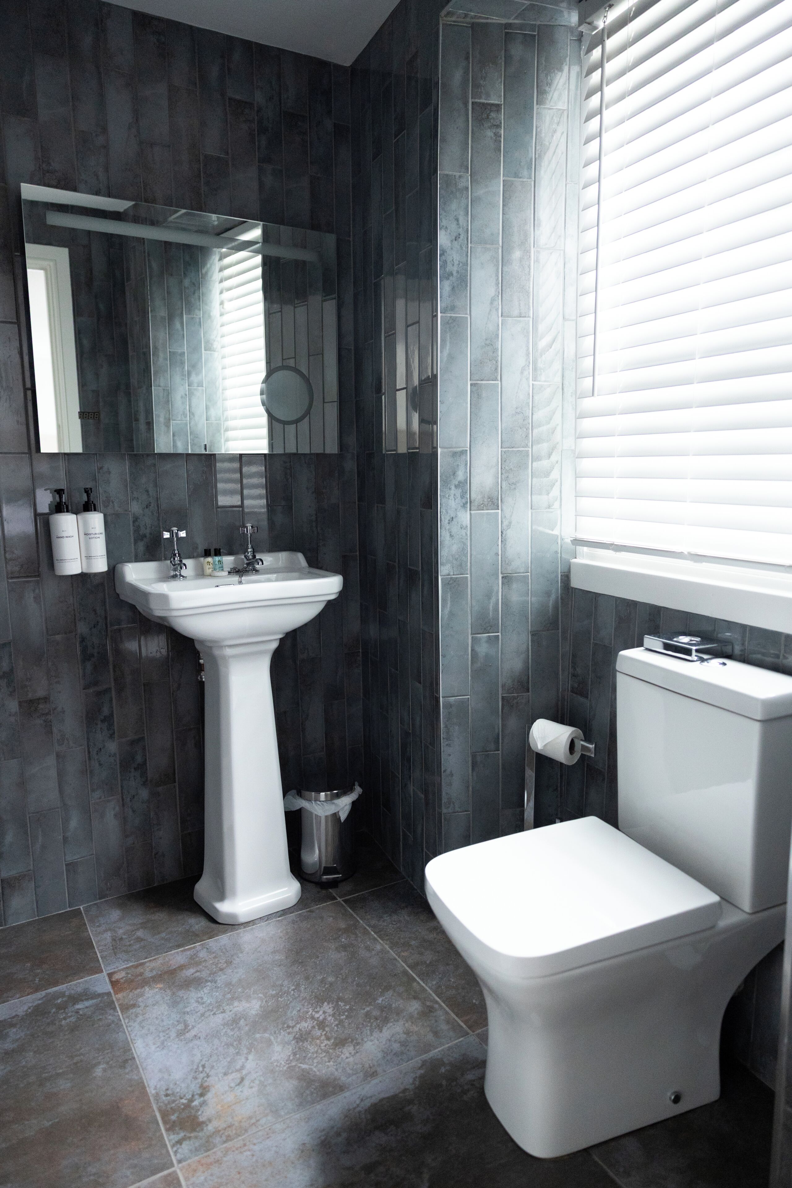 A bathroom with a pedestal sink, toilet, and a mirror above the sink.