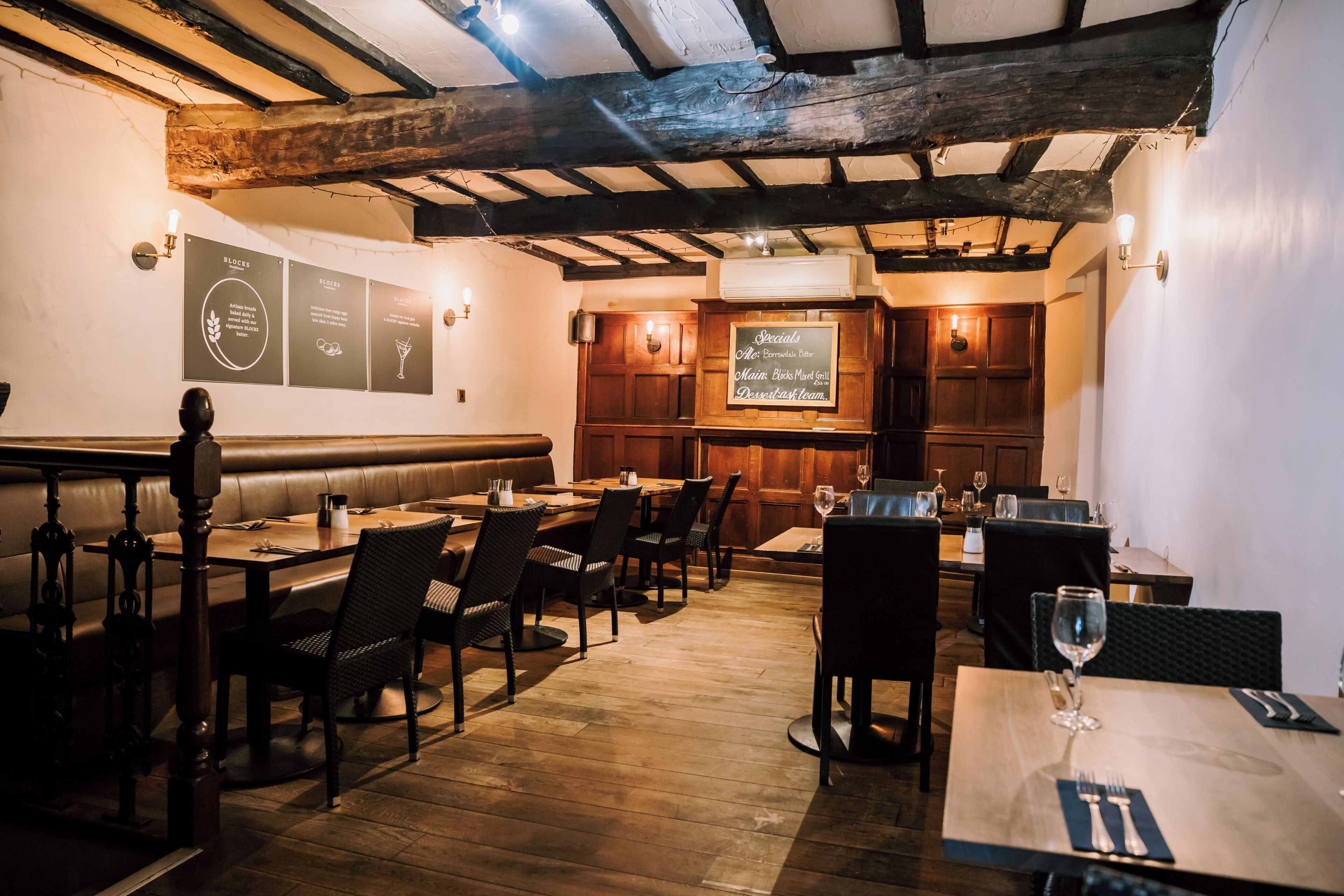 A restaurant with wooden beams, tables, chairs, and a menu board.