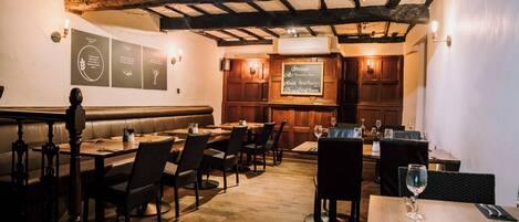 A restaurant with wooden beams, tables, chairs, and a menu board.