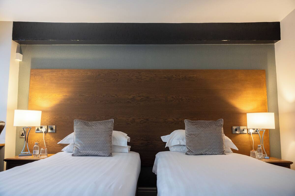 Una habitación de hotel con dos camas, cada una con almohada y una mesita de noche con lámpara.