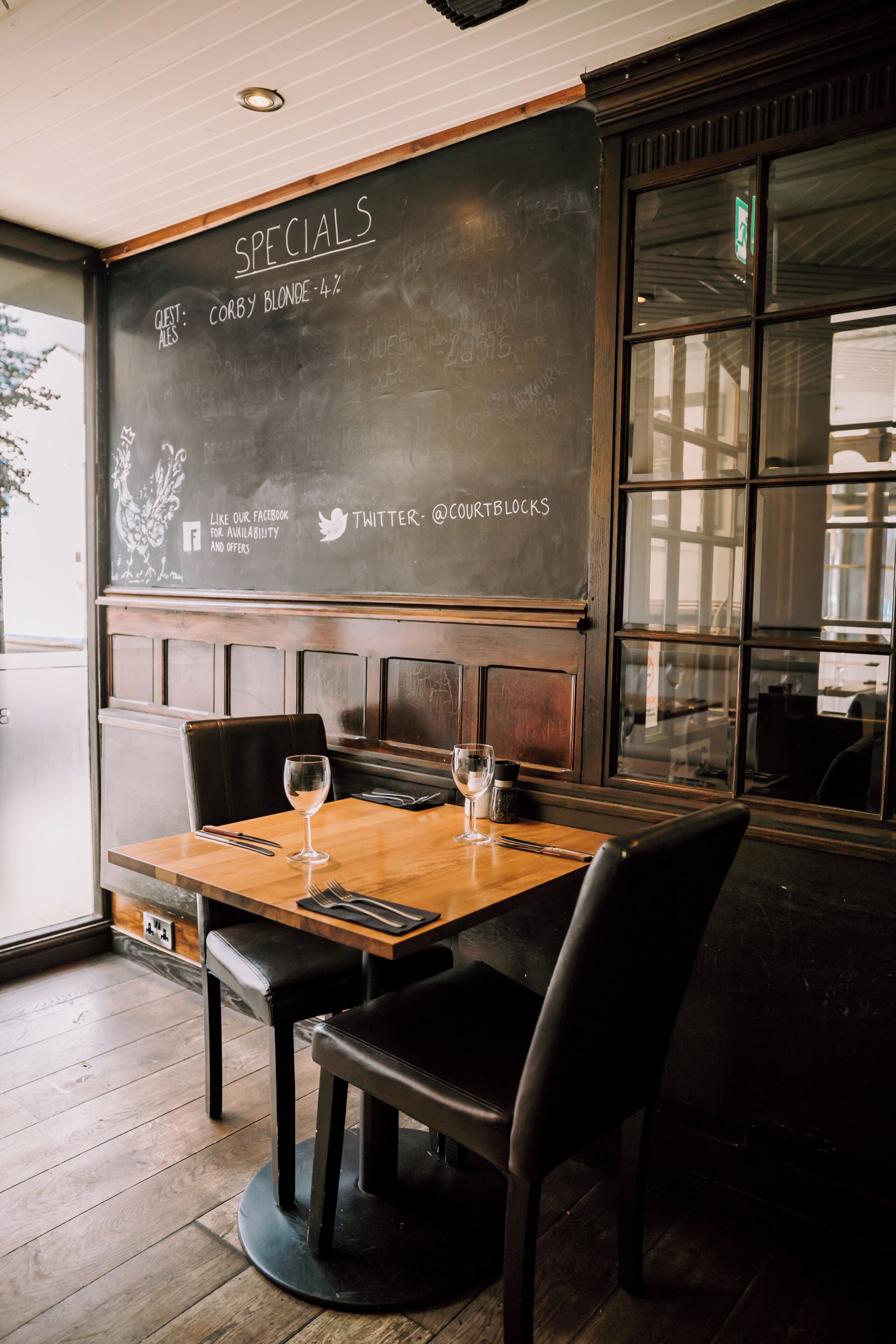 A restaurant interior with a chalkboard menu, wooden table, black chairs, and a window view.