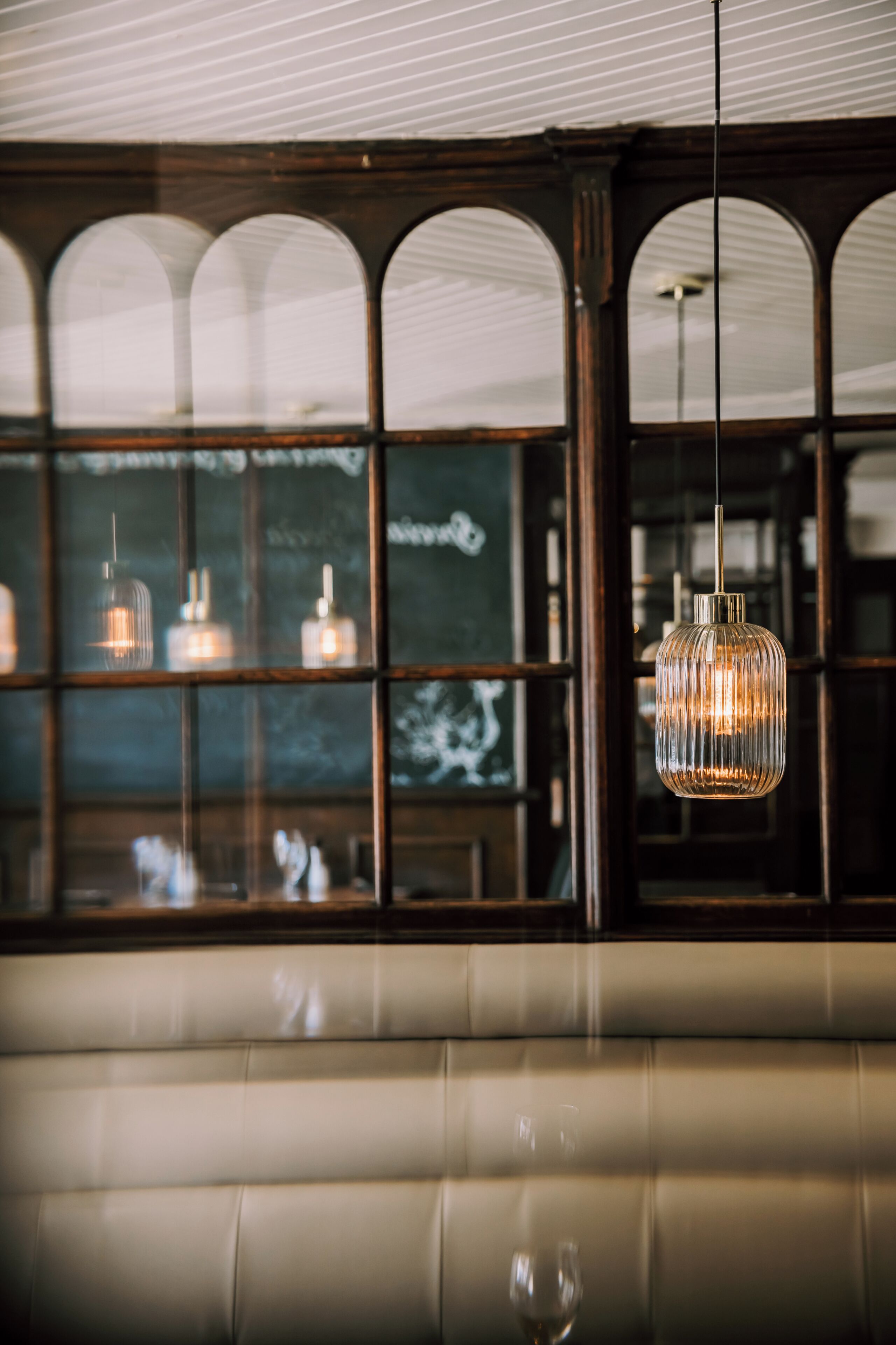 Een restaurantinterieur met een zithoek met perken, gebogen ramen en hangende吊り灯.