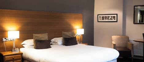A hotel room with a large bed, two bedside lamps, a chair, and a framed picture on the wall.