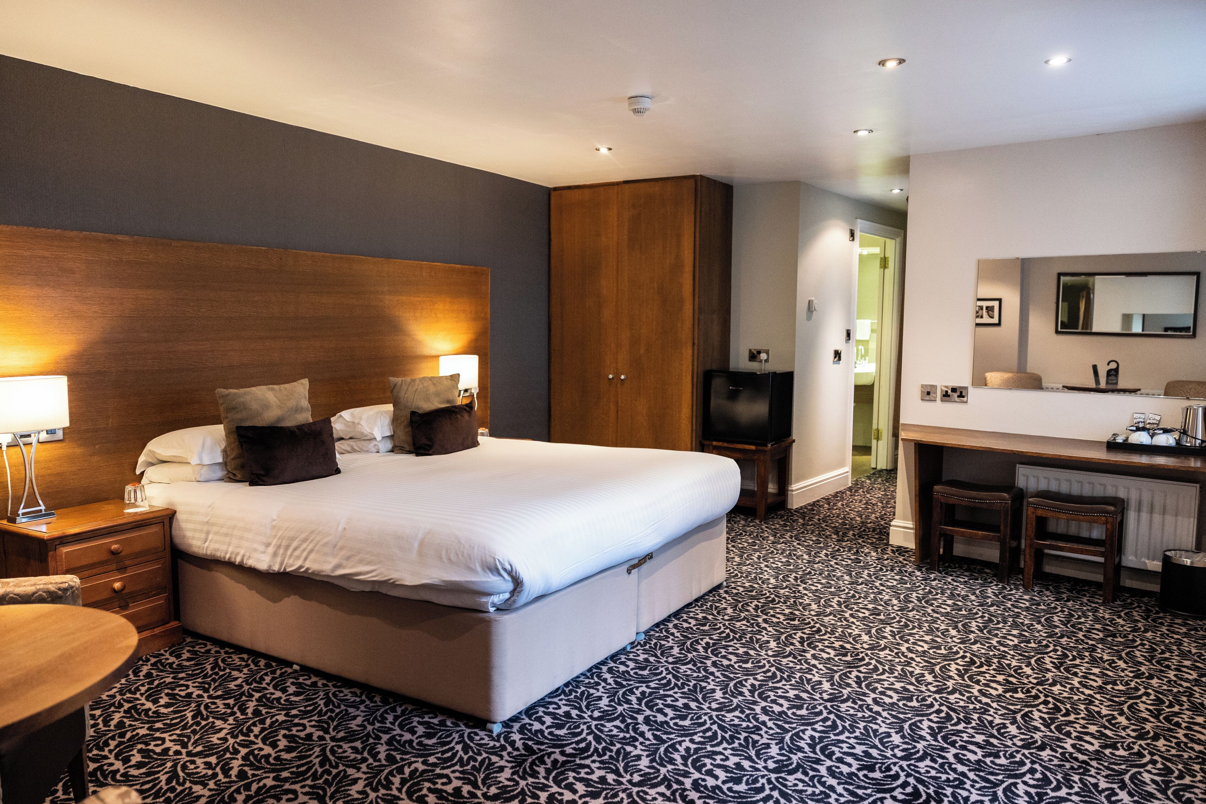 A hotel room with a large bed, bedside tables, a desk, a chair, a mirror, and a television.