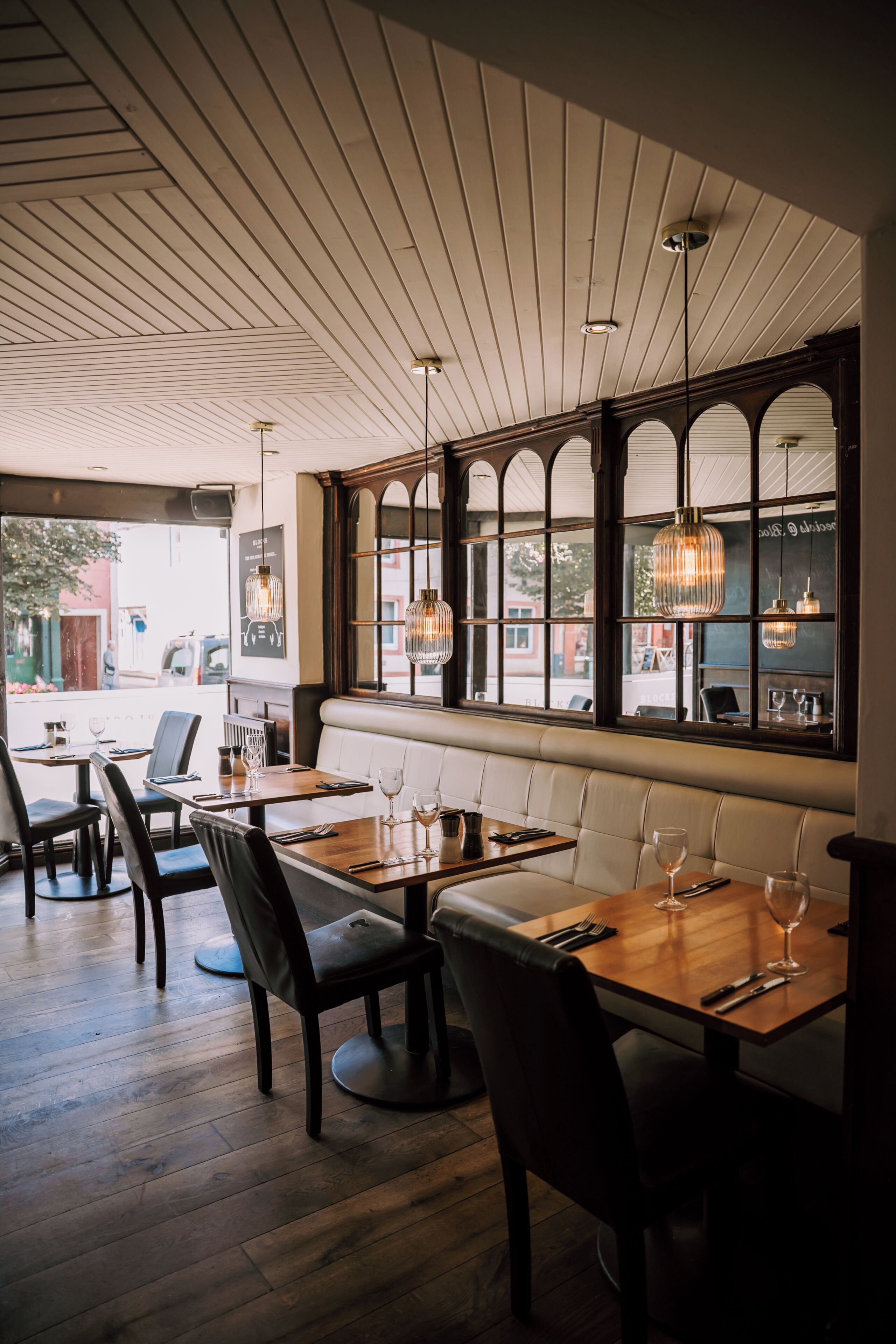 A restaurant interior with wooden tables, leather seating, and large windows with arched tops.
