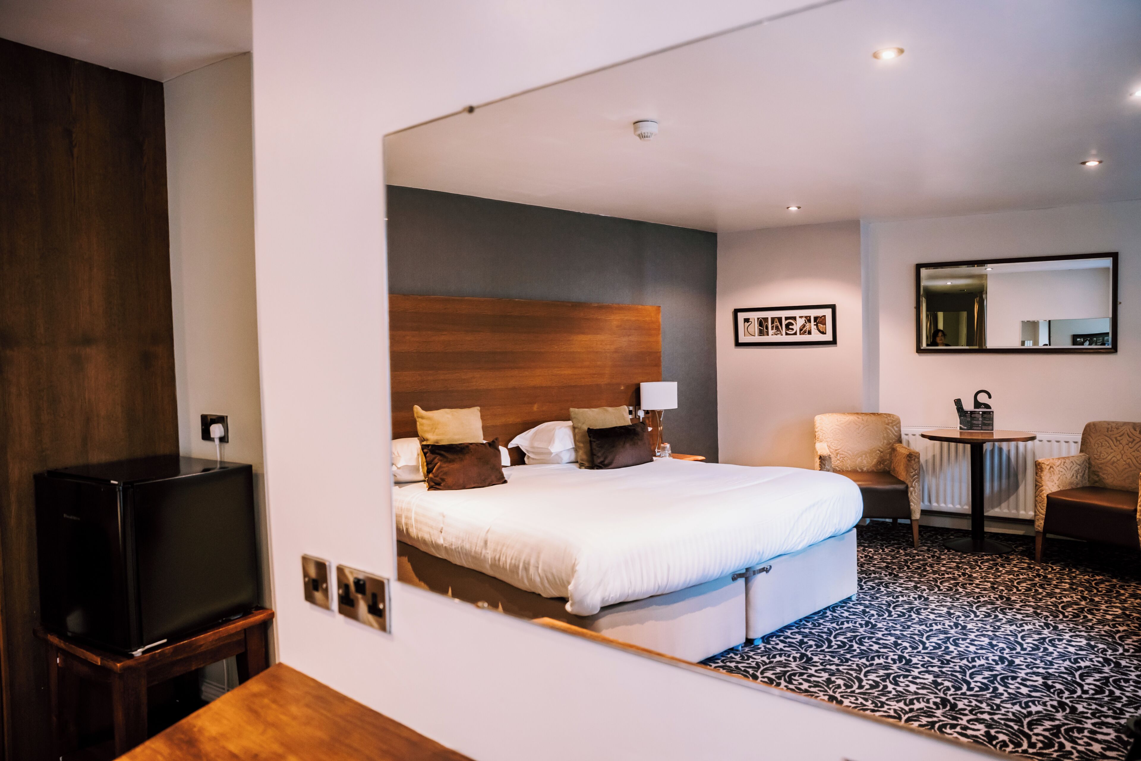 A hotel room with a bed, a television, a chair, a table, and a mirror.
