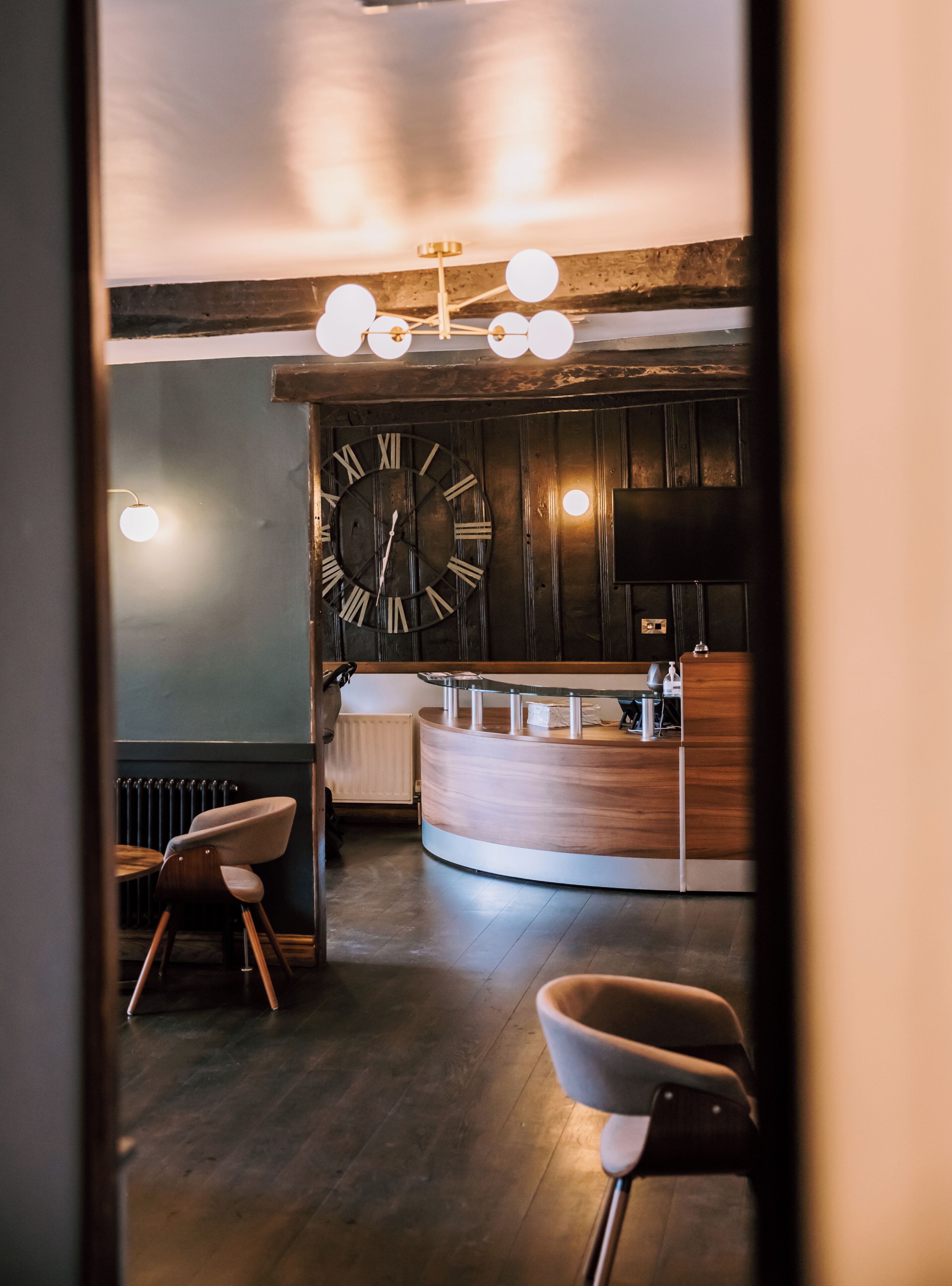 A reception area with a wooden reception desk, a large wall clock, and a modern light fixture.