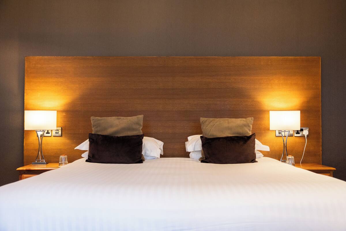 Una habitación de hotel con una cama grande, dos mesitas de noche, lámparas y un cabecero de madera.