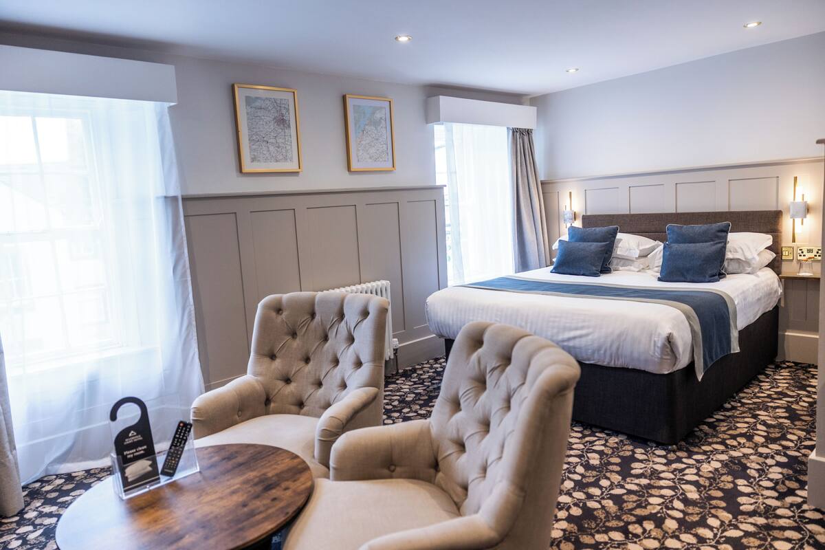 Una habitación de hotel con una cama, dos sillones, una mesita redonda y un radiador.