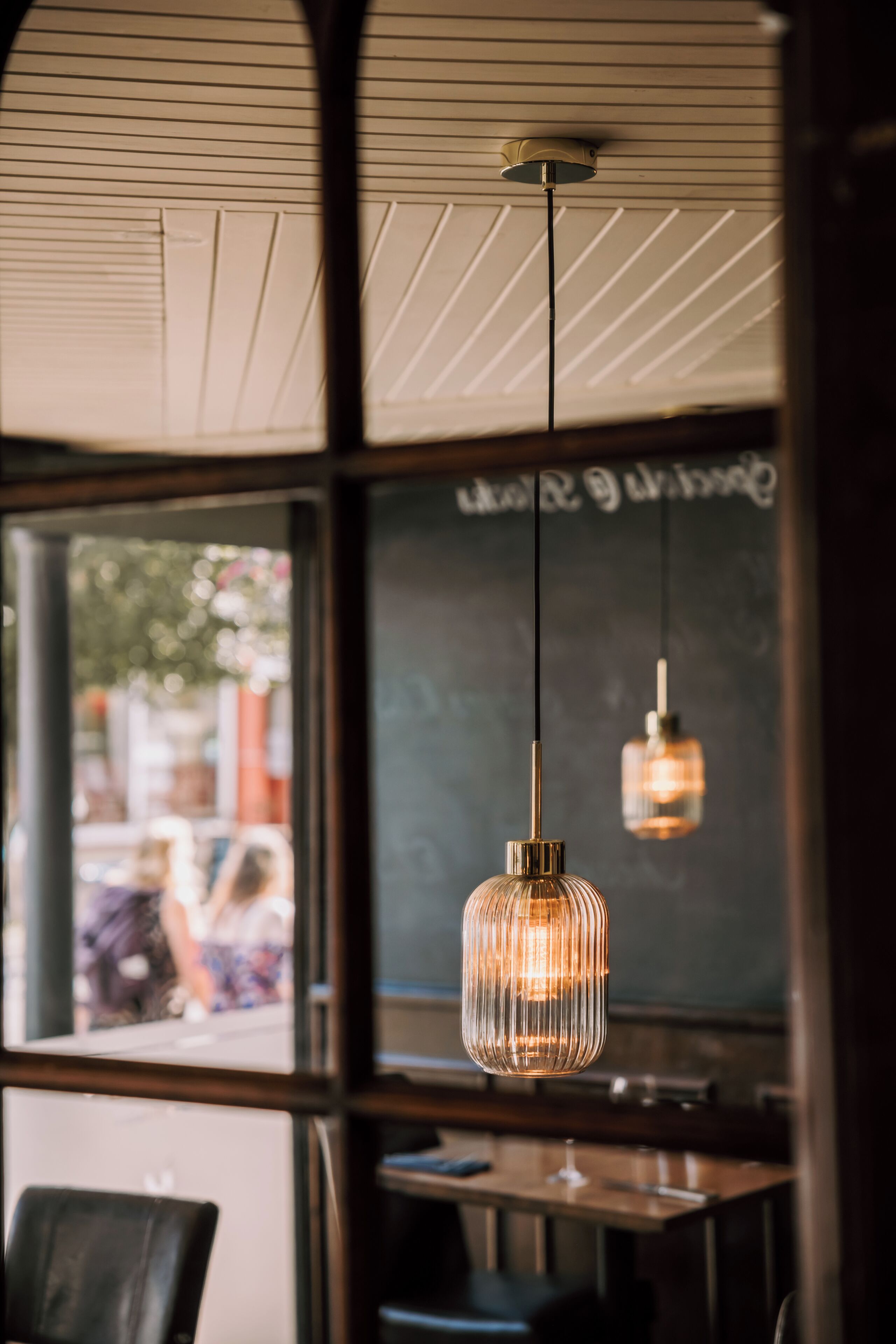 A restaurant interior with a chalkboard menu, hanging pendant lights, and a view through the window.